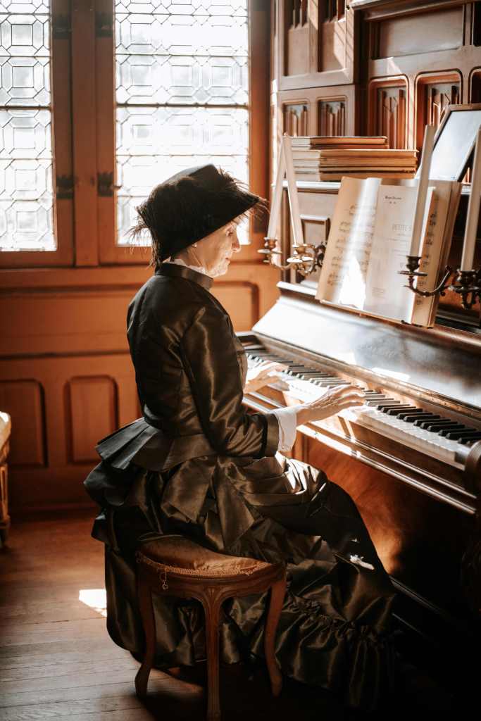 Femme en robe à tournure au château de Josselin dans le Morbihan, jouant du piano